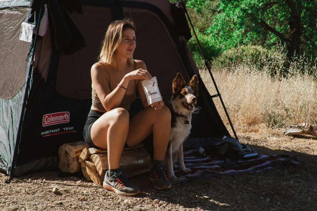 Eine Frau sitzt mit ihrem Hund im Eingang ihres Zeltes und isst eine packung CBD Gummibärchen