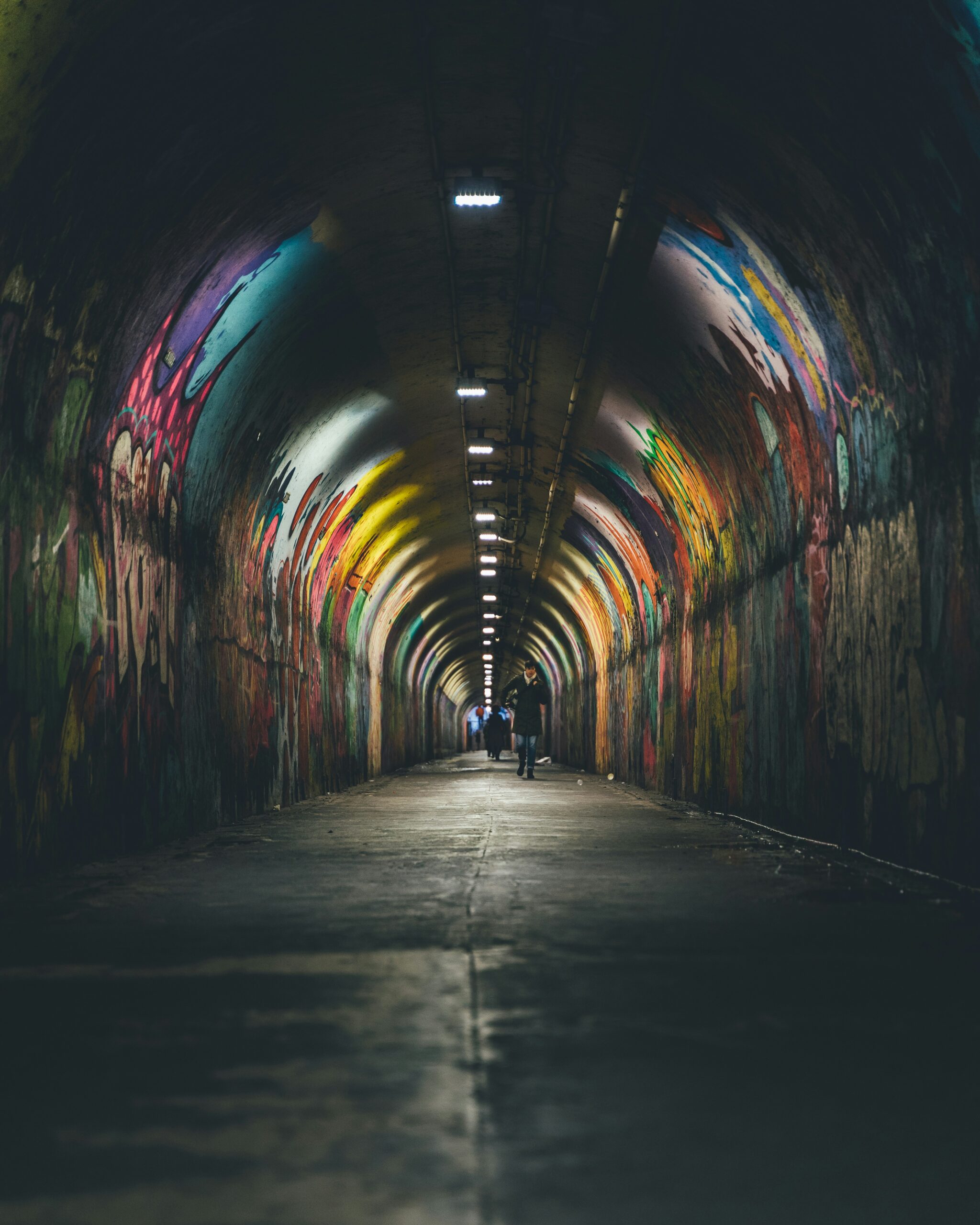 Zwei Menschen gehen durch einen leicht beleuchteten mit Graffiti besprühten Tunnel. Es soll widerspiegeln, dass sich Menschen mit Morbus Crohn oft sozial isolieren.