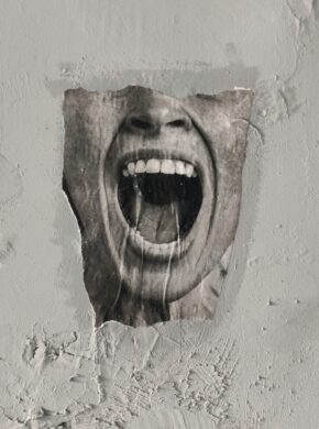Braunes menschliches Gesicht aus Holz geschnitzt an der Wand. Der Mund ist weit aufgerissen und erinnert an einen Schrei, der an das Tourette-Syndrom erinnert. Betroffene können ihre Tics nicht kontrollieren.