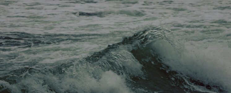 Das Bild zeigt den Ausschnitt von einem unruhigen Meer. Große Steine liegen im Wasser und es baut sich eine kleine Welle auf. Das erinnert an den schwankenden Blutzuckerspiegel bei einer Diabetes-Erkrankung.